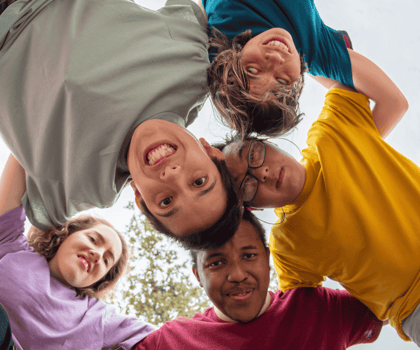 Groep jonge mensen met en zonder beperking lacht samen in een cirkel, symbool voor inclusie en verbondenheid.