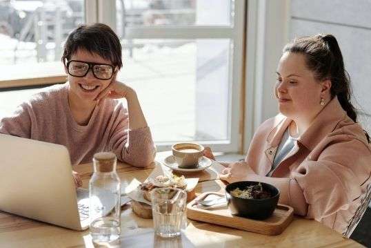 Twee meisjes aan tafel met koffie en een laptop