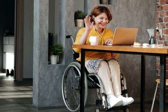 Vrouw in rolstoel zwaait naar de camera van haar laptop