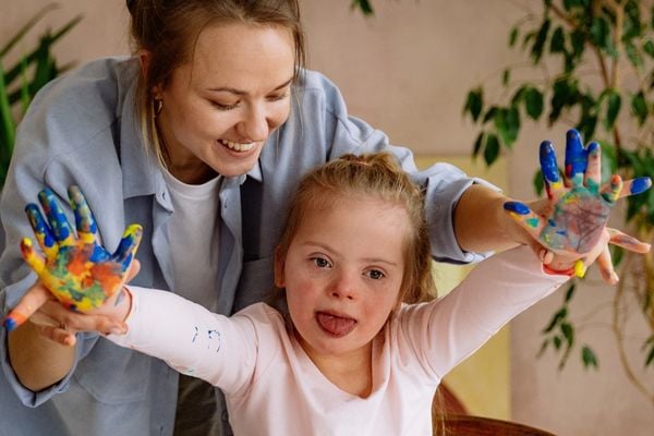 Assistent helpt met schilderen met kindje met Downsyndroom