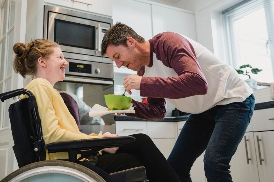 Une jeune femme en fauteuil roulant est aidée par son assistante pendant qu'elle mange