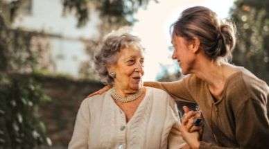 Une personne âgée et une jeune femme s'embrassent dans un parc avec un sourire au visage