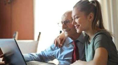 Opa en kleindochter zitten samen achter de laptop aan een tafel